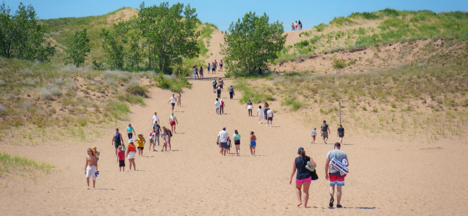 The Sleeping Bear Dunes height is one of those facts that sounds made up until you are standing at the base looking up and wondering what life decisions brought you to this moment. These dunes rise up to 450 feet above Lake Michigan — that is taller than a 40-story building — making them among the highest freshwater coastal dunes on the planet. I have stood at the top with wind whipping sand into my face and watched grown adults sit down mid-descent and refuse to move. I have also watched kids sprint up like mountain goats while their parents quietly reconsidered their fitness levels. Whether you are here for the views, the geology, or simply to prove something to yourself, understanding the scale of what you are looking at changes everything about the experience. Located inside Sleeping Bear Dunes National Lakeshore on the northwestern coast of Michigan's Lower Peninsula, these ancient glacial giants are unlike anything else in the Midwest.